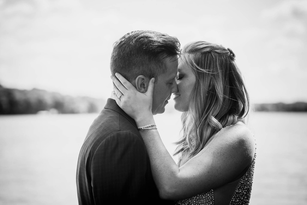 Bride pulling groom in for intimate kiss in front of lake